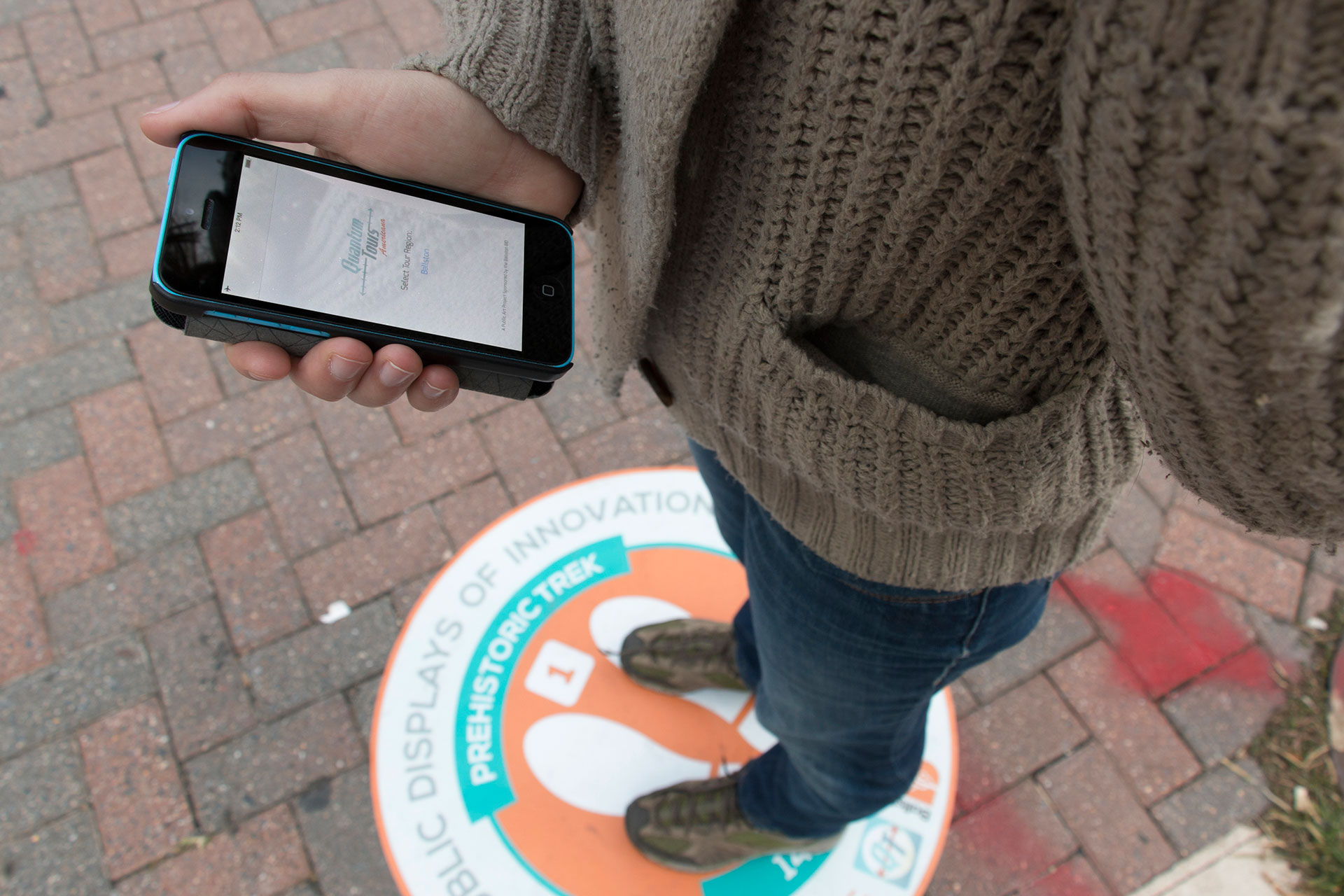 A photo of a woman holding a smartphone while standing on a round sidewalk decal.